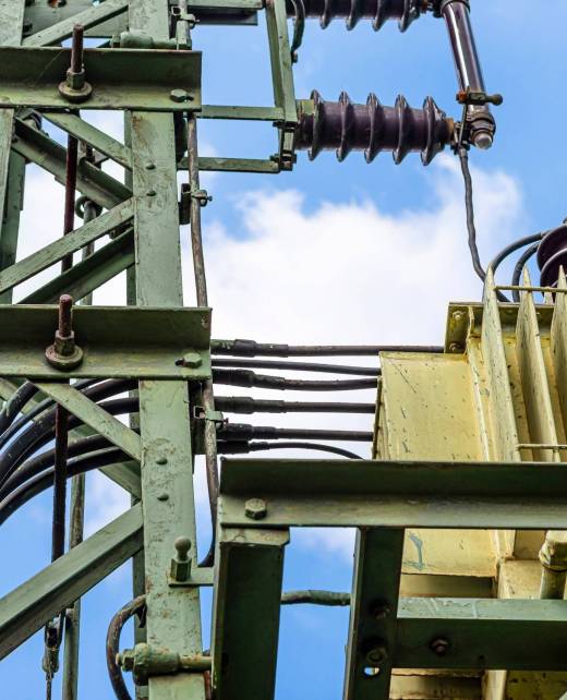 Green electric pole with a transformer standing next to railway tracks, used to distribute voltage on railway lines.